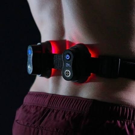 A person is sitting comfortably on a couch with a red light therapy device wrapped around their knee, utilizing medical grade laser technology to relieve joint pain and reduce inflammation. This effective tool is part of their pain management routine, aimed at improving blood flow and stimulating healing in chronic conditions.