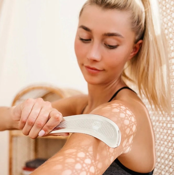 A person is applying gel to their lower leg, preparing for muscle scraping with a metal tool, a technique often used for muscle recovery to relieve pain and improve blood flow. This process helps to promote healing in sore muscles and connective tissues, supporting recovery from tightness and stiffness.