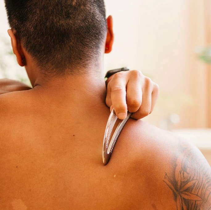 A person is using a stainless steel scraping tool on their calf muscle, applying pressure to address soft tissue restrictions and promote healing. This technique, often associated with the Graston technique, is a form of manual therapy aimed at reducing pain and improving mobility.